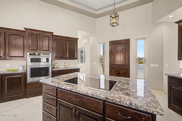 The chef's kitchen is an entertainer's dream, featuring two granite islands, rich dark wood cabinetry stacked to soaring tray ceilings, SS appliances including double wall ovens and a cooktop, all bathed in natural light from a stunning band of clerestory windows. From the kitchen, unobstructed desert and mountain views pour through every window, keeping you connected to the breathtaking landscape while you cook and gather.