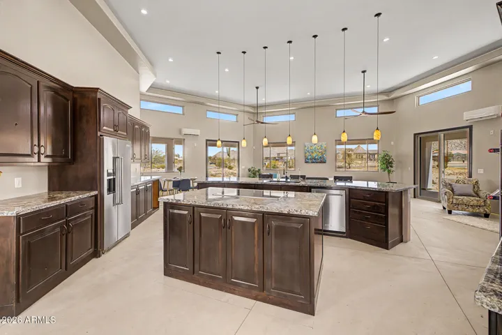 The chef's kitchen is an entertainer's dream, featuring two granite islands, rich dark wood cabinetry stacked to soaring tray ceilings, SS appliances including double wall ovens and a cooktop, all bathed in natural light from a stunning band of clerestory windows. From the kitchen, unobstructed desert and mountain views pour through every window, keeping you connected to the breathtaking landscape while you cook and gather.