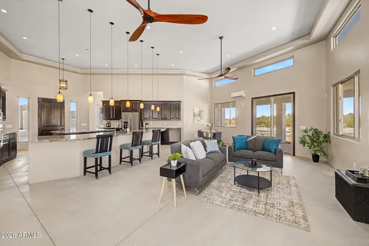 The great room is the heart of this home, effortlessly flowing from a sun-drenched breakfast nook to a defined dining area and comfortable sitting space, all anchored by soaring tray ceilings, designer ceiling fans, and warm pendant lighting. Floor-to-ceiling windows frame sweeping desert and mountain views from every angle, making every meal and moment feel like you're living inside the landscape.