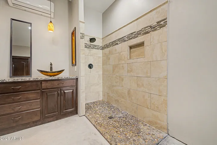 The primary bath stuns with dual artisan vessel sinks on a granite vanity, warm pendant lighting, a custom tile walk-in shower with pebble stone flooring