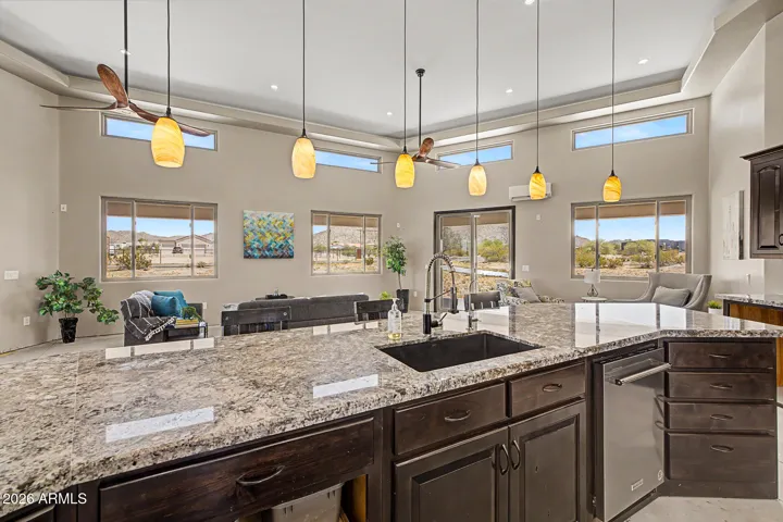 The chef's kitchen is an entertainer's dream, featuring two granite islands, rich dark wood cabinetry stacked to soaring tray ceilings, SS appliances including double wall ovens and a cooktop, all bathed in natural light from a stunning band of clerestory windows. From the kitchen, unobstructed desert and mountain views pour through every window, keeping you connected to the breathtaking landscape while you cook and gather.