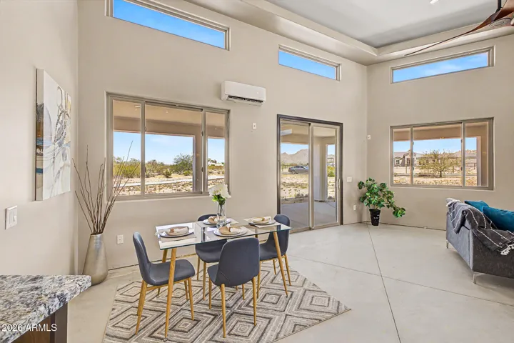 The great room is the heart of this home, effortlessly flowing from a sun-drenched breakfast nook to a defined dining area and comfortable sitting space, all anchored by soaring tray ceilings, designer ceiling fans, and warm pendant lighting. Floor-to-ceiling windows frame sweeping desert and mountain views from every angle, making every meal and moment feel like you're living inside the landscape.