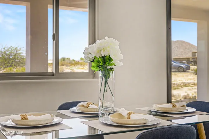 The great room is the heart of this home, effortlessly flowing from a sun-drenched breakfast nook to a defined dining area and comfortable sitting space, all anchored by soaring tray ceilings, designer ceiling fans, and warm pendant lighting. Floor-to-ceiling windows frame sweeping desert and mountain views from every angle, making every meal and moment feel like you're living inside the landscape.