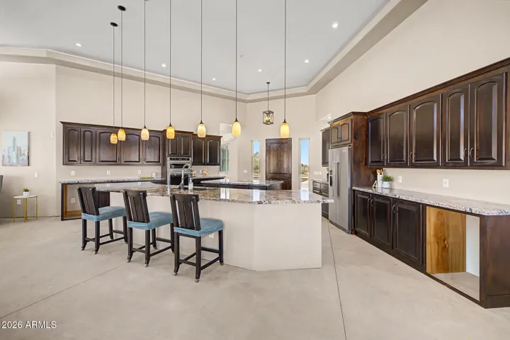 The chef's kitchen is an entertainer's dream, featuring two granite islands, rich dark wood cabinetry stacked to soaring tray ceilings, SS appliances including double wall ovens and a cooktop, all bathed in natural light from a stunning band of clerestory windows. From the kitchen, unobstructed desert and mountain views pour through every window, keeping you connected to the breathtaking landscape while you cook and gather.