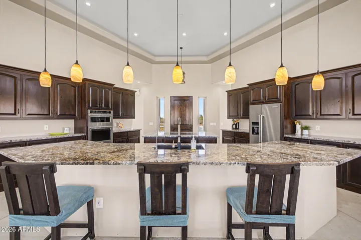 The chef's kitchen is an entertainer's dream, featuring two granite islands, rich dark wood cabinetry stacked to soaring tray ceilings, SS appliances including double wall ovens and a cooktop, all bathed in natural light from a stunning band of clerestory windows. From the kitchen, unobstructed desert and mountain views pour through every window, keeping you connected to the breathtaking landscape while you cook and gather.
