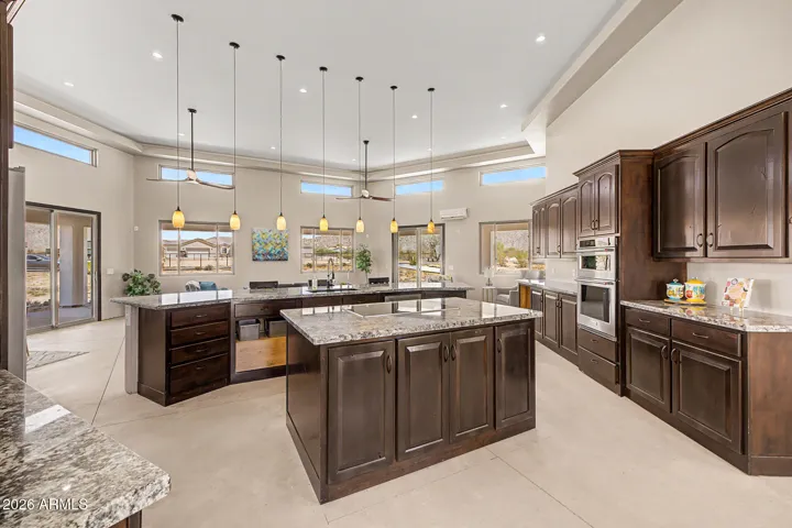 The chef's kitchen is an entertainer's dream, featuring two granite islands, rich dark wood cabinetry stacked to soaring tray ceilings, SS appliances including double wall ovens and a cooktop, all bathed in natural light from a stunning band of clerestory windows. From the kitchen, unobstructed desert and mountain views pour through every window, keeping you connected to the breathtaking landscape while you cook and gather.