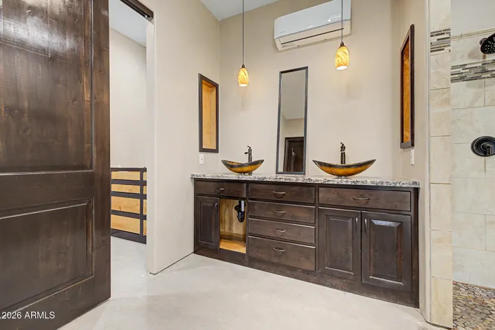 The primary bath stuns with dual artisan vessel sinks on a granite vanity, warm pendant lighting, a custom tile walk-in shower with pebble stone flooring