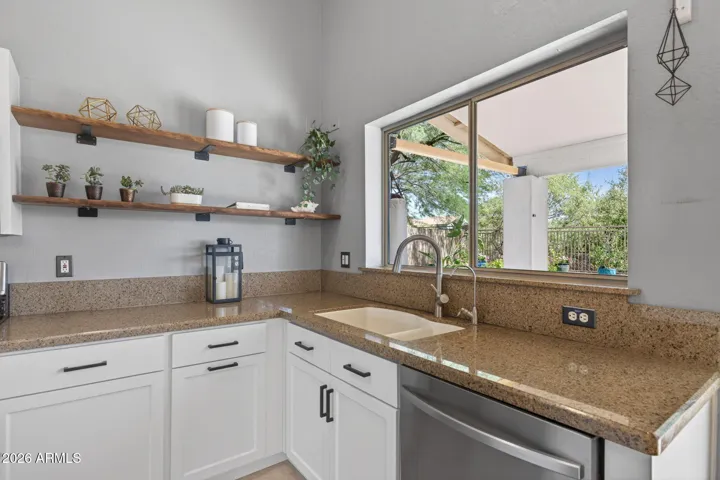 A large window in the kitchen brings in plenty of natural light, complementing open shelving and high ceilings.