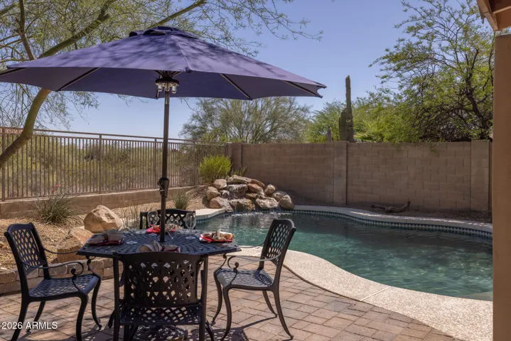 Resort-style backyard featuring a sparkling pool with rock waterfall, expansive paver patio, and desert views