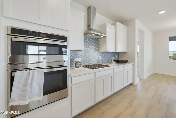 GOURMET KITCHEN WITH PAINTED CABINETS, QUARTZ COUNTERS, DESIGNER BACKSPLASH, GAS COOKTOP, BUILT-IN OVENS AND DESIGNER HOOD.