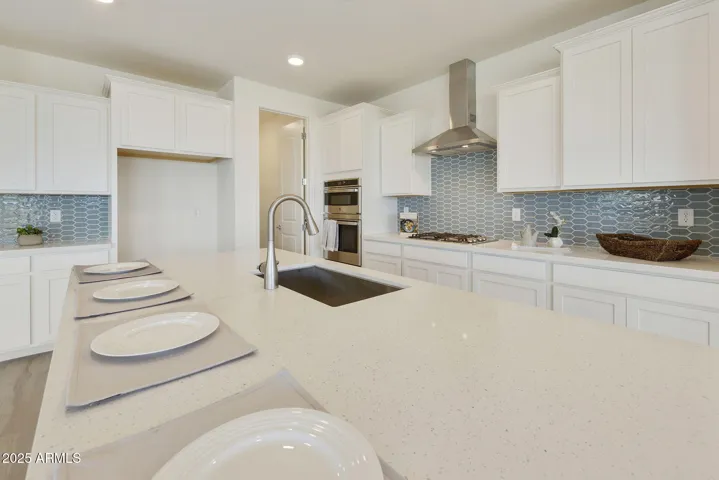 GOURMET KITCHEN WITH PAINTED CABINETS, QUARTZ COUNTERS, DESIGNER BACKSPLASH, GAS COOKTOP, BUILT-IN OVENS AND DESIGNER HOOD.