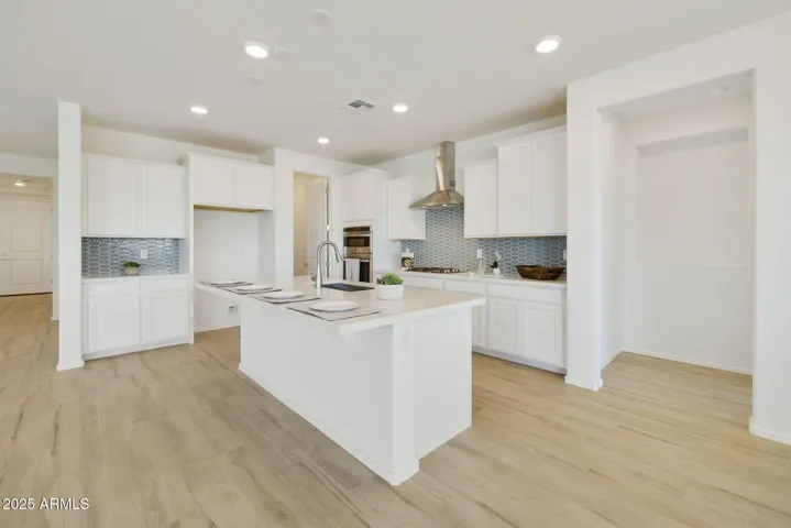 GOURMET KITCHEN WITH PAINTED CABINETS, QUARTZ COUNTERS, DESIGNER BACKSPLASH, GAS COOKTOP, BUILT-IN OVENS AND DESIGNER HOOD.