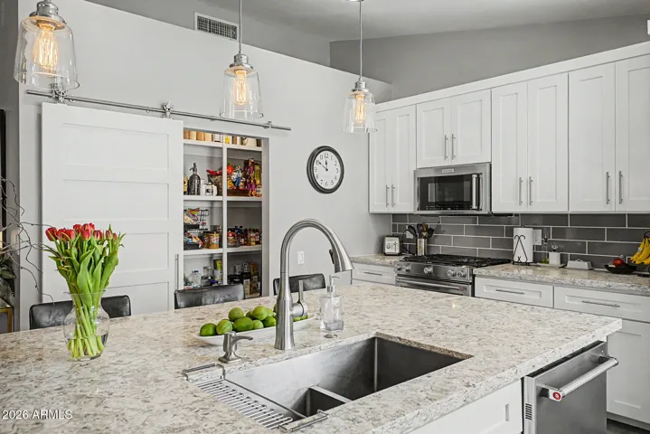 Walk-in pantry with sliding barn door and built-in shelving for added storage. Modern finishes throughout with tile flooring, recessed lighting, and neutral tones