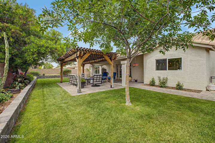 Framed by mature trees and a custom wood pergola, this backyard offers layered outdoor spaces with a perfect blend of sun and shade.