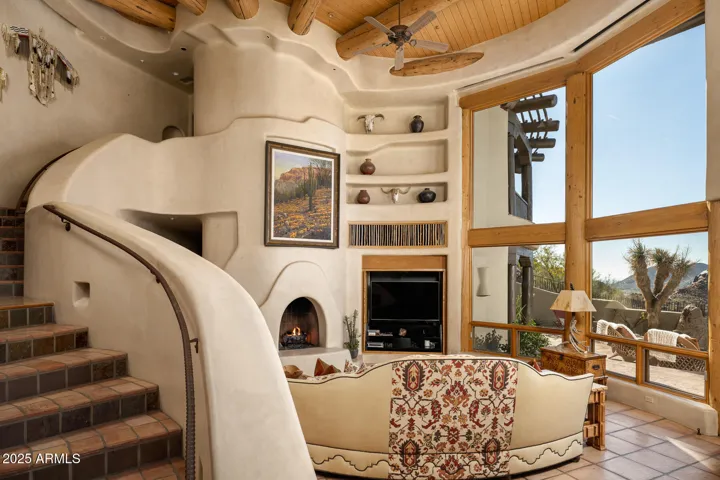 The secondary family room blends rustic elegance with dramatic design elements, including a curved plaster fireplace, tall ceilings with log beams, and large windows that bring in natural light and outdoor views.
