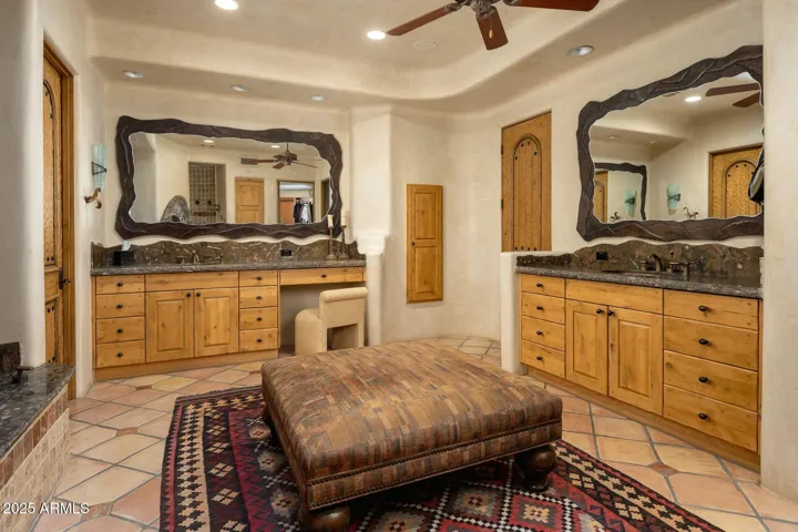 This spacious primary bathroom in Paradise Valley offers dual vanities with granite countertops, custom wood cabinetry, and unique framed mirrors. The layout emphasizes luxury and functionality with separate prep areas and warm natural tones, making it the perfect private retreat
