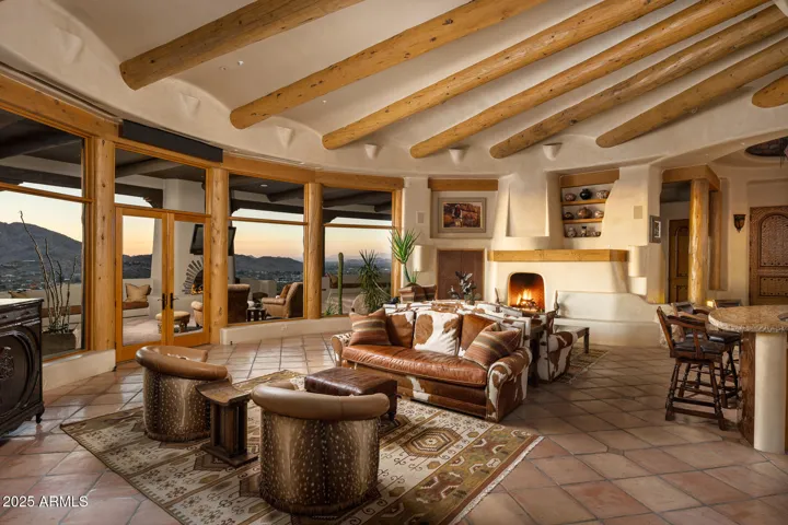This luxurious living area blends rustic charm and elegance with a large kiva-style fireplace, exposed wood beams, and curved architecture. The open design allows for easy flow between indoor and outdoor spaces, maximizing comfort and visual appeal.