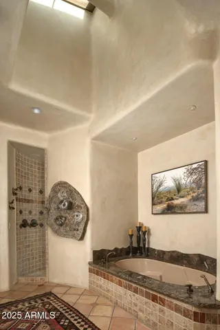 Relax in the stunning primary bath complete with a deep soaking tub, natural stone finishes, and a custom rain shower set into a tile alcove. Vaulted ceilings and rich textures enhance the spa-like atmosphere of this upscale Paradise Valley home.