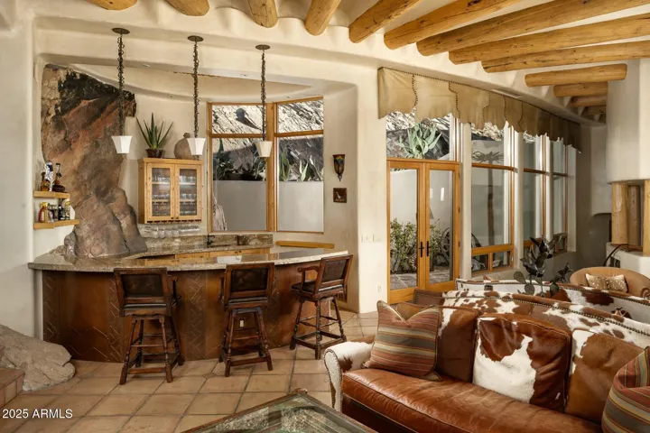 This spacious great room offers luxurious comfort with a built-in wet bar featuring natural stone accents and custom cabinetry. Large windows overlook a tranquil Zen garden, bringing serene desert landscaping indoors. Perfect for hosting in style in your Paradise Valley estate.