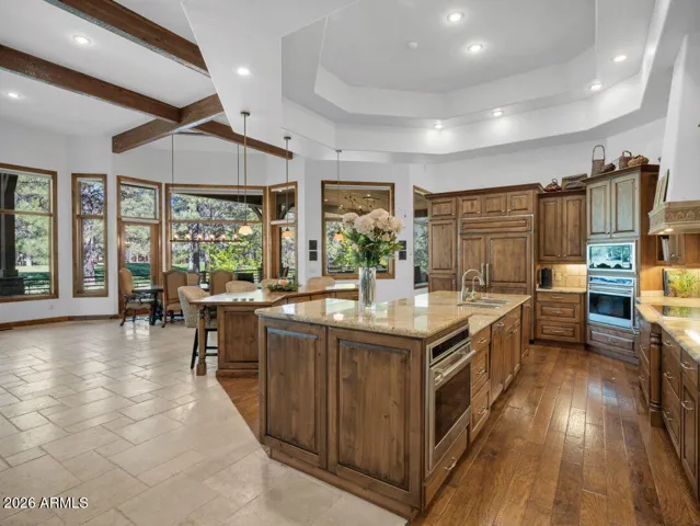 Spacious great room with exposed beams, stone fireplace, built-in entertaining area, and oversized windows capturing scenic golf course and forest views.