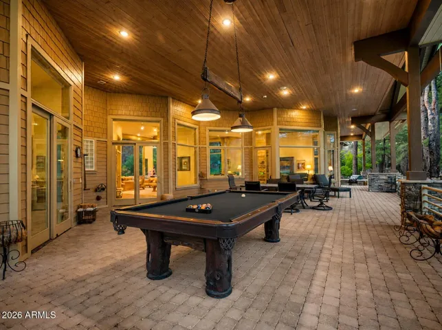 Incredible 1,600-square-foot covered patio with outdoor entertaining space, custom pool table, fireplace seating, and seamless indoor-outdoor living overlooking the golf course.