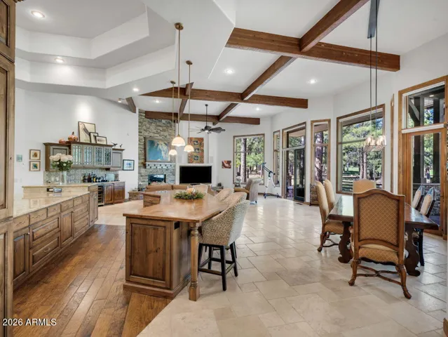 Spacious open-concept kitchen and living area with exposed wood beams, oversized windows, custom cabinetry, and seamless indoor-outdoor flow overlooking the pine forest setting.
