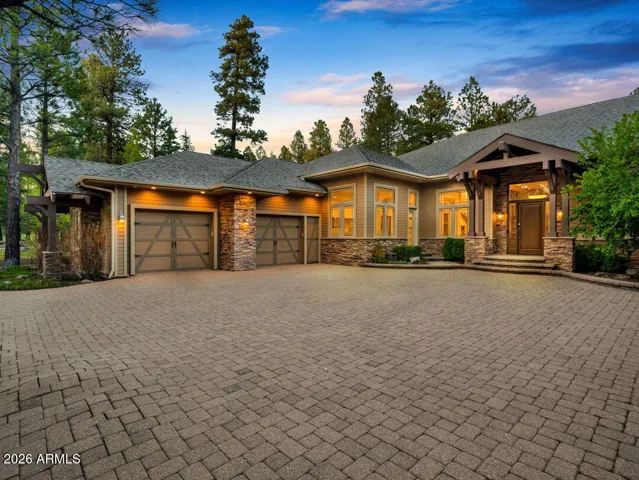 Luxury home exterior featuring a heated 5-car garage with EV charging, custom garage doors, and an oversized driveway surrounded by mature pine trees in Forest Highlands.