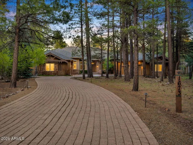 Stunning luxury home nestled among towering pine trees with a long paver driveway, beautiful stone accents, and exceptional curb appeal in Flagstaff.