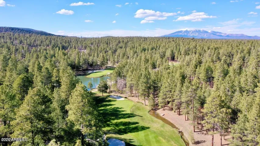 Spectacular aerial view showcasing rolling golf course fairways, water features, dense pine forests, and mountain vistas throughout Flagstaff.