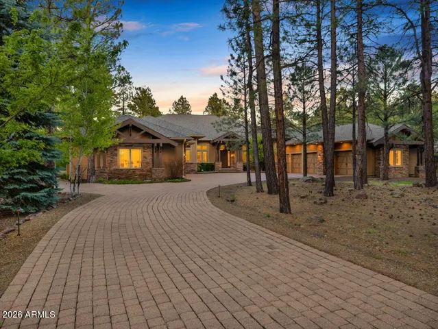 Beautifully designed mountain home entrance surrounded by towering pines, showcasing elegant stone accents, custom architecture, and a welcoming private driveway in Flagstaff.