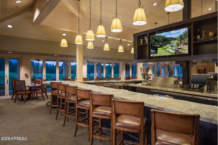 Elegant clubhouse bar and lounge area featuring granite countertops, warm wood finishes, and expansive golf course views through oversized windows in Flagstaff.