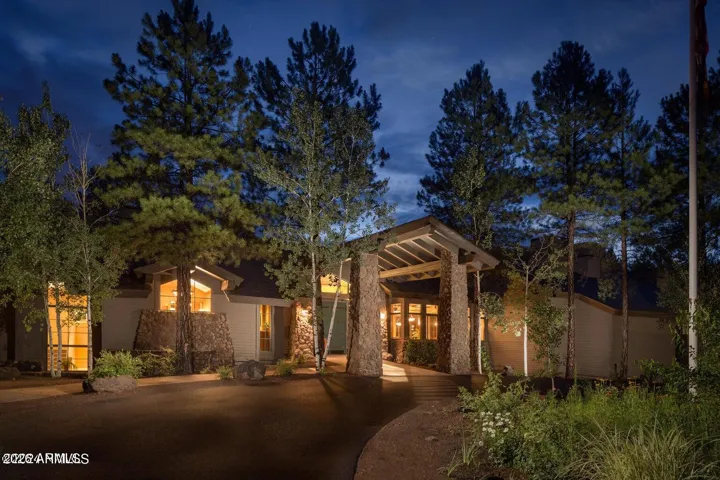 Beautifully illuminated clubhouse exterior with rustic stone architecture and welcoming curb appeal surrounded by peaceful pine forest scenery.