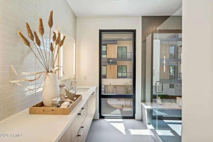 The primary bath delivers a spa-like experience with dual vanities, illuminated mirrors, quartz countertops, and a striking tile accent wall, all designed with a modern, sophisticated aesthetic.