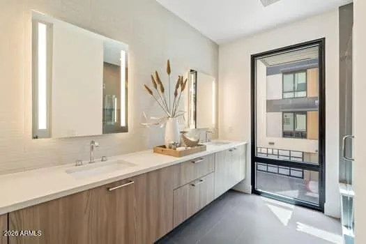 The primary bath delivers a spa-like experience with dual vanities, illuminated mirrors, quartz countertops, and a striking tile accent wall, all designed with a modern, sophisticated aesthetic.