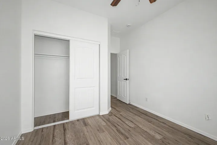 Bright bedroom features hard wood flooring, neutral paint, ceiling fan, window for natural light, and closet; minimal and move-in ready.