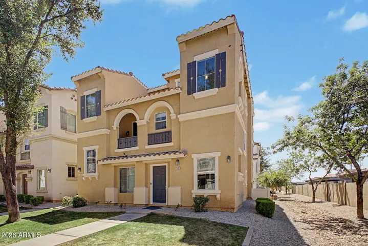 Front exterior of townhouse featuring stucco finish, tile roof, arched architectural details, private fenced yard, and covered patio.