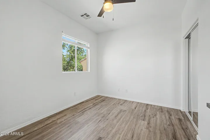 Bright bedroom features hard wood flooring, neutral paint, ceiling fan, window for natural light, and closet; minimal and move-in ready.