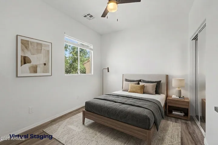 Bright bedroom features hard wood flooring, neutral paint, ceiling fan, window for natural light, and closet; minimal and move-in ready.