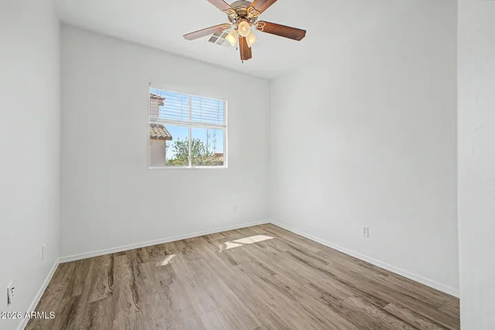 Bright bedroom features hard wood flooring, neutral paint, ceiling fan, window for natural light, and closet; minimal and move-in ready.