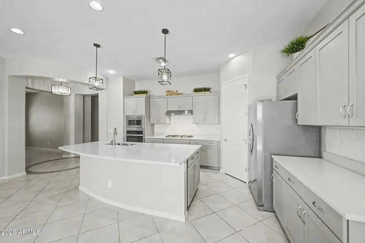 This modern kitchen boasts a large curved quartz waterfall island, sleek grey shaker cabinetry, integrated stainless steel appliances, and distinctive cage pendant lighting and a pantry