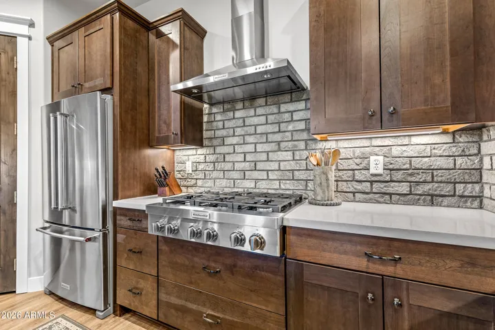Beautiful mountain modern back-splash highlights stainless gas stove, vent hood and refrigerator.