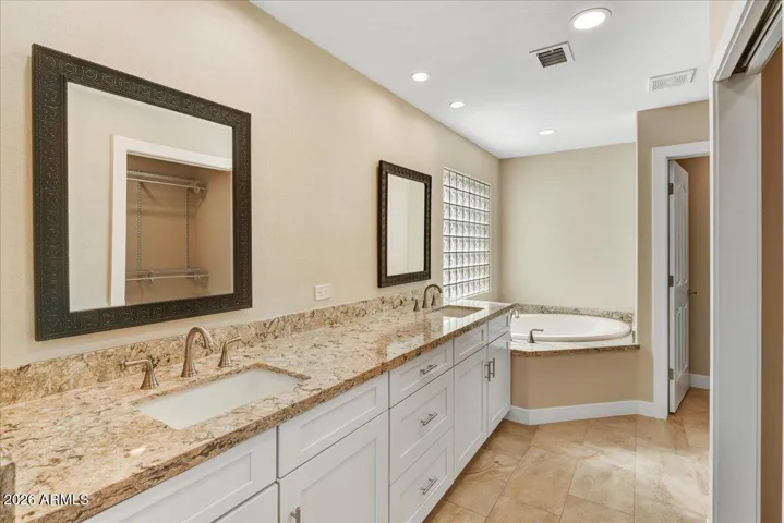 Primary bathroom with granite counters, white cabinets, double vanity, tile walk-in shower and soaker tub