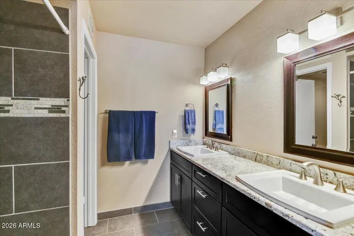 Primary bathroom features double sinks with updated granite counters, cabinets and tile walk-in shower
