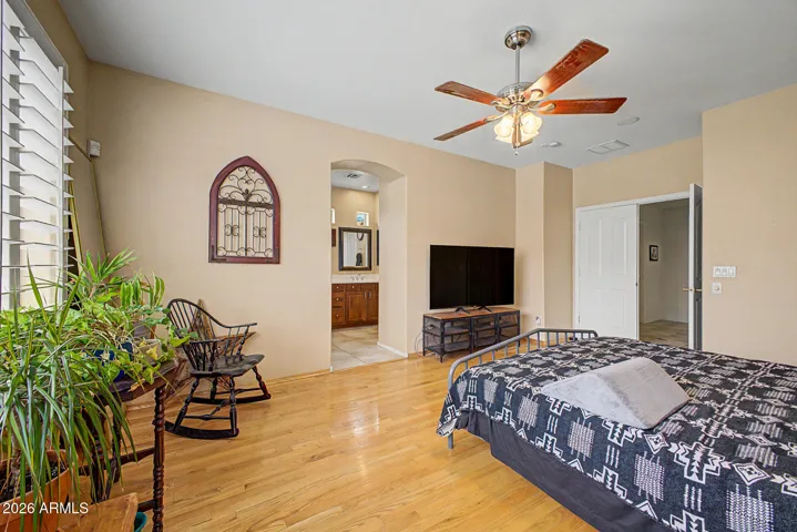 Primary retreat with real wood floors, ceiling fan, and plantation shutters opens to an upgraded bath retreat
