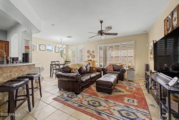 Open great room with dining area features patio access, upgraded tile floors, plantation shutters, ceiling fan, dining chandelier, and built-in audio.
