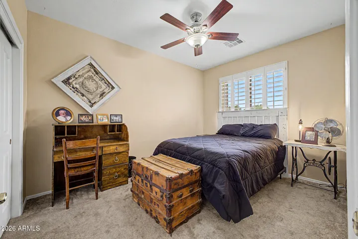 Comfortable guest bedroom with plantation shutters and ceiling fan reflects the home’s consistent attention to detail.