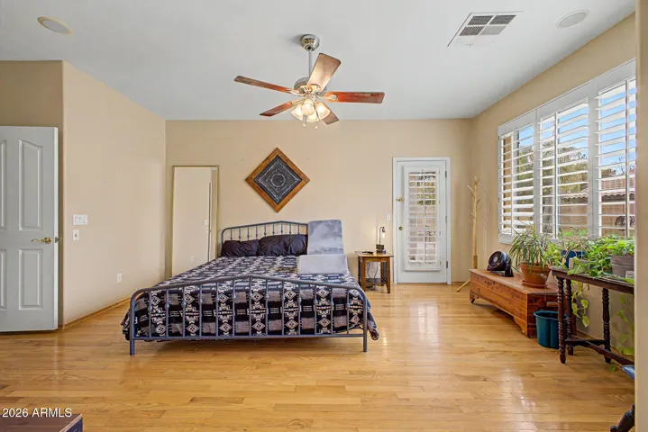 Primary suite features real hardwood floors, plantation shutters, and ceiling fan, with direct access to a spa-inspired bath showcasing an oversized walk-in shower with rainhead.
