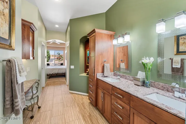 Rich alder wood cabinetry anchors dual vanities, complemented by a generous linen closet and a dedicated seated makeup area—where beauty meets effortless organization.