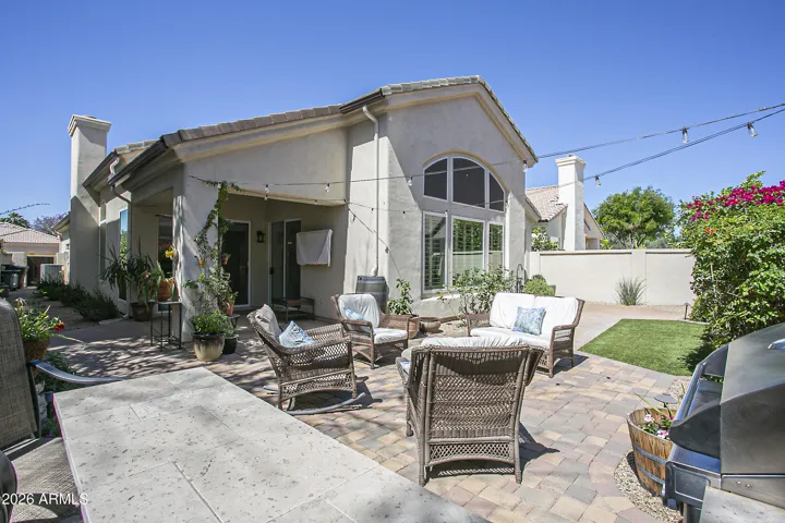 A quiet, relaxing backyard featuring a gas BBQ, gas firepit, covered patio, faux grass, and beautiful plantings.