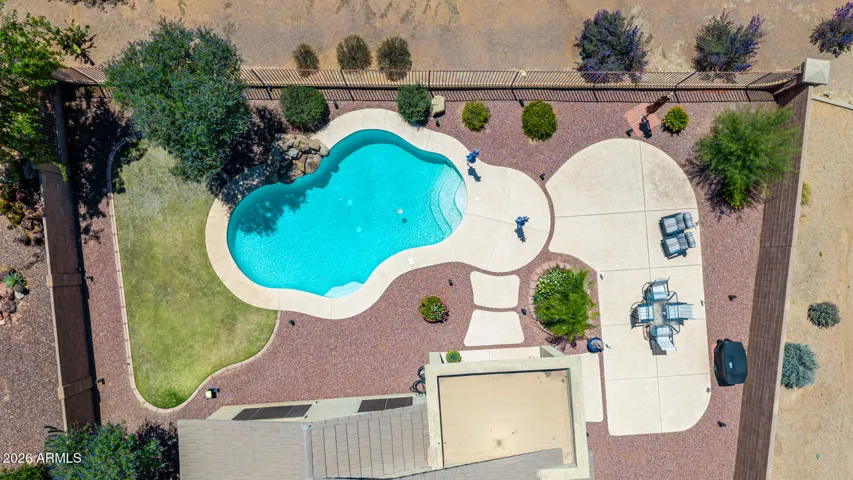 A drone view of the backyard showcases the lush green grass, the sparkling pool, and the spacious patio.